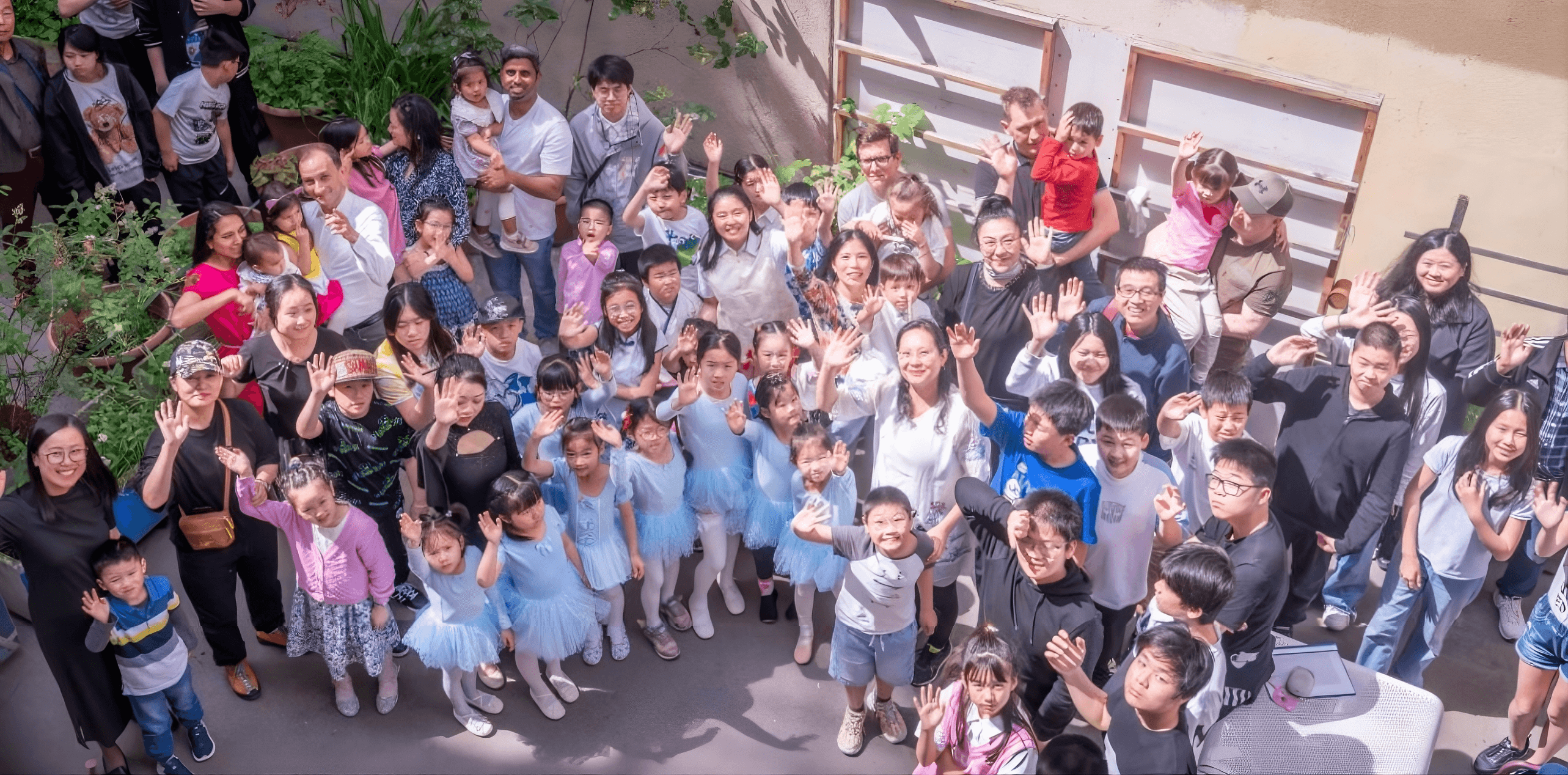 Schülerinnen, Schüler und Familien der Aohua Chinesischschule winken gemeinsam im Hof.